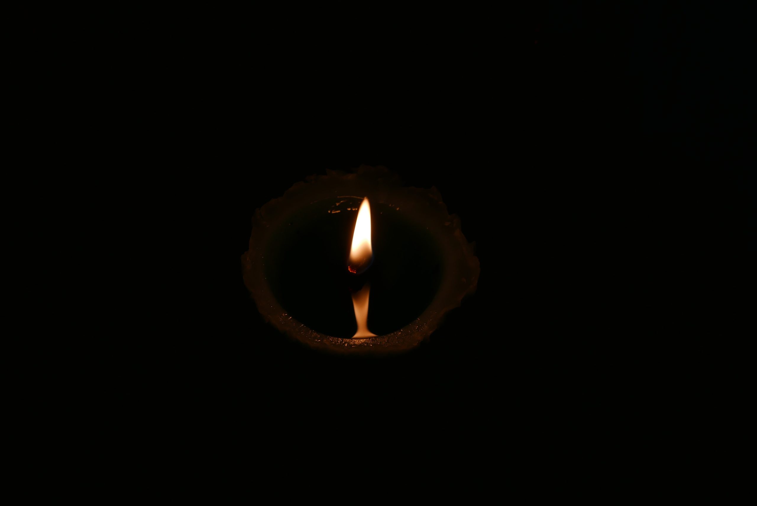 Schwache Flamme einer Kerze in der Dunkelheit